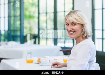 Frau mittleren Alters sitzt beim Frühstück im Café mit Kaffee, Gebäck und Orangensaft, Kopierraum Stockfoto