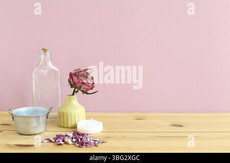 Aromatherapie-Objekte. Glasflasche, getrocknete Rosenblume, Kerze auf Holztisch mit pinkfarbenem Hintergrund Stockfoto