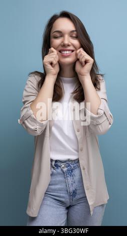 Lächelnde brünette junge Frau in Hemd und Jeans auf blauem Hintergrund Stockfoto