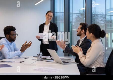 Eine Geschäftsfrau präsentiert sich während eines Meetings, während ihre Kollegen ihre Anerkennung für ihren Beitrag zum Team klatschen. Sie feiern den Erfolg. Stockfoto