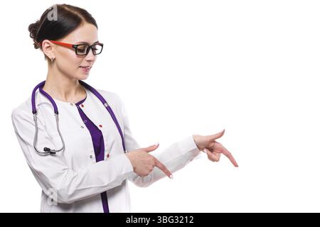 Porträt der jungen attraktiven kaukasischen brünetten lächelnden Ärztin, die im Büro steht und in weißer Uniform mit leerem Bereich wegschaut Stockfoto