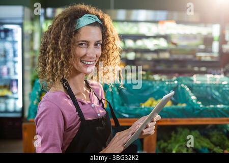 Frau mit schwarzer Schürze, die Tablette hält, während sie Kisten im Lebensmittelbereich, im Kopierraum stopft Stockfoto