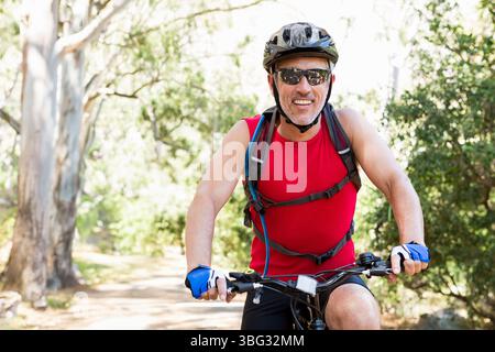 Senior Mann, der auf dem Waldweg Mountainbike fährt, mit Helm Sonnenbrille Handschuhen Hydration Pack Stockfoto