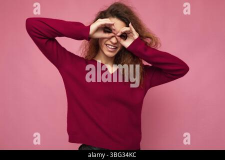 Porträt von jungen positiven glücklich fröhlich schöne Brünette lockig Frau mit aufrichtigen Emotionen tragen trendige rosa Pullover isoliert auf rosa Hintergrund Stockfoto