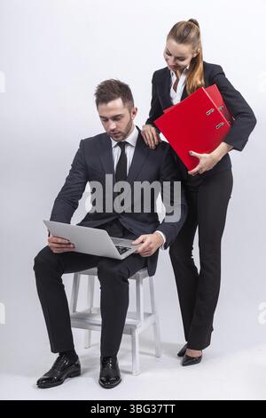 Ein paar schöne junge kaukasische Bürofrau mit Pferdeschwanz in schwarzem Anzug mit Mappen in den Händen und Manager-Mann in schwarzem Anzug, der mit Laptop I sitzt Stockfoto