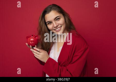 Junge schöne europäische stilvolle Brünette Frau trägt weiße Bluse und rote Strickjacke isoliert auf rotem Hintergrund mit positiven aufrichtigen Emotionen. Hol Stockfoto