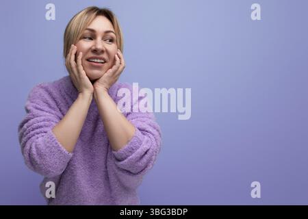 Porträt der traumhaften charmanten niedlichen blonden Frau im Lavendelpullover auf lila Hintergrund mit Kopierraum Stockfoto