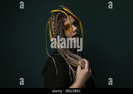 Eine Frau mit Dreadlocks steht vor einem grünen Hintergrund. Sie blickt mit einem neutralen Ausdruck in die Kamera, ihr Haar kaskadiert d Stockfoto