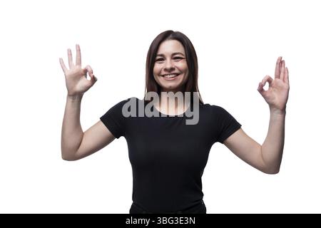 Weiße süße junge Frau mit schwarzem Haar, die ein schwarzes T-Shirt trägt, zeigt eine ausgezeichnete Geste Stockfoto