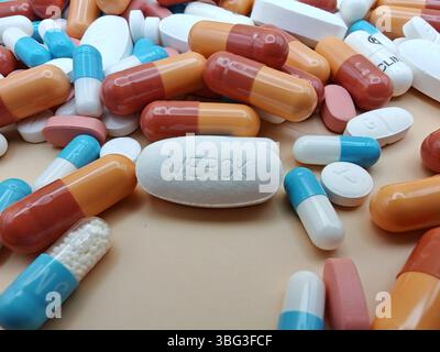 Weiße Pille mit MERCK-Aufdruck auf Tablettenstapel und farbenfrohe Kapseln in pharmazeutischer Optik. Stockfoto