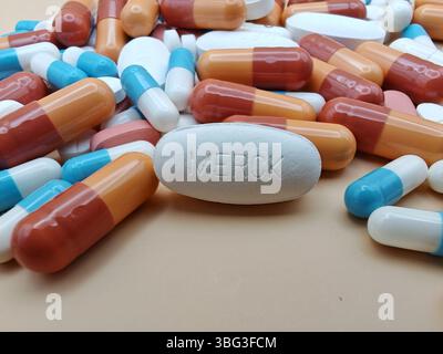 Weiße Pille mit MERCK-Aufdruck auf Tablettenstapel und farbenfrohe Kapseln in pharmazeutischer Optik. Stockfoto