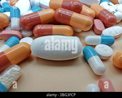 Weiße Pille mit MERCK-Aufdruck auf Tablettenstapel und farbenfrohe Kapseln in pharmazeutischer Optik. Stockfoto
