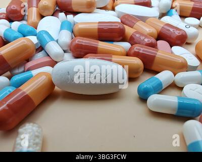Weiße Pille mit MERCK-Aufdruck auf Tablettenstapel und farbenfrohe Kapseln in pharmazeutischer Optik. Stockfoto