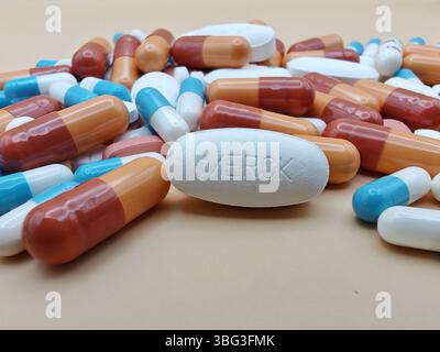 Weiße Pille mit MERCK-Aufdruck auf Tablettenstapel und farbenfrohe Kapseln in pharmazeutischer Optik. Stockfoto