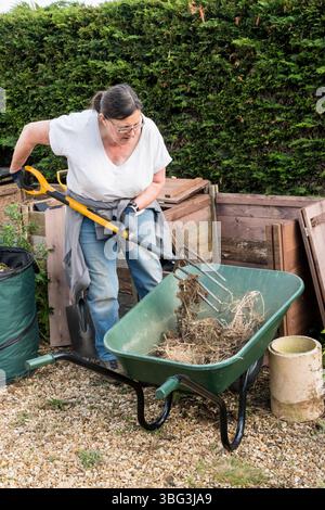 Frau, die im Garten arbeitet und Kompost zwischen den Mülleimern bewegt. Stockfoto