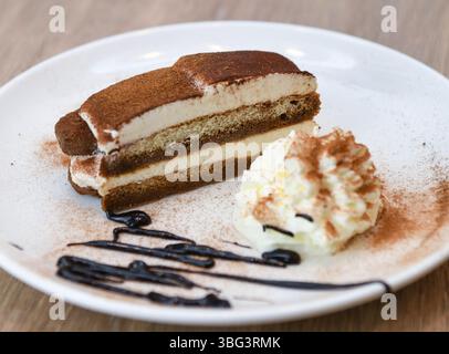 Tiramisu-Kuchen mit Schlagsahne und Schokoladensauce auf weißem Teller Stockfoto