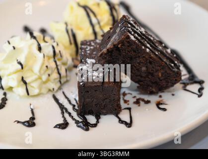 Schokoladen-Brownies mit Schlagsahne und Vanilleeis auf weißem Teller Stockfoto