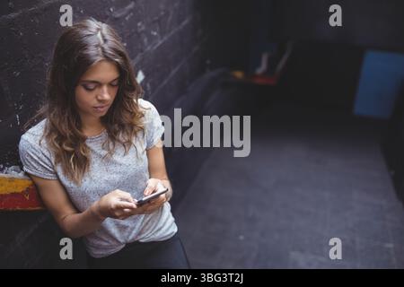 Frau Mitte 20 lehnte sich an die bemalte Wand in der städtischen Gasse und hielt Smartphone in der Nähe von Felsvorsprung, Kopierraum Stockfoto