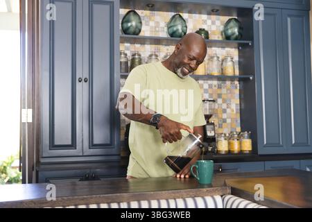 Ranghoher Afroamerikaner, der in der Küche steht und Kaffee aus der französischen Presse in eine grüne Tasse gießt Stockfoto