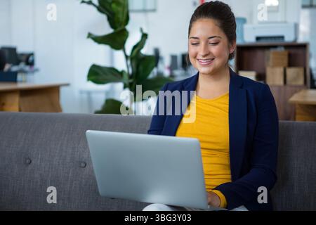Frau, die auf einem grauen Sofa in der modernen Bürolounge sitzt und Geschäftskleidung trägt Stockfoto