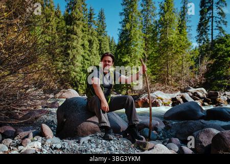Mann Tourist sitzt auf Stein am Seeufer in den Bergen Stockfoto