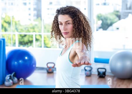 Frau balanciert in Yoga-Pose auf blauer Trainingsmatte im Studio mit Kettlebells und Stabilitätsball Stockfoto