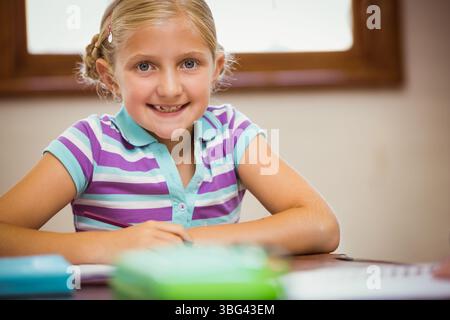 Schulmädchen lächelt und sortiert bunte Notizbücher und Bleistiftetui auf einem Holztisch im Arbeitszimmer Stockfoto