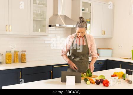 Hauskoch hackt grünen Paprika auf weißer Quarzplatte in der Küche mit Tablettenständer Stockfoto
