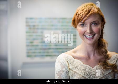 Rothaarige Frau mit cremefarbener Spitze oben stehend, lächelnd vor verschwommenen Kunstwerken in der modernen Galerie Stockfoto