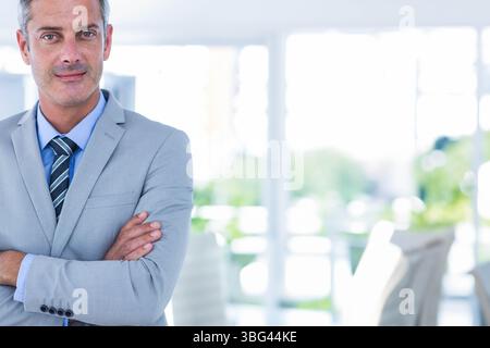 Mann mit Anzugsjacke, gestreifter Krawatte, die Arme im Konferenzraum an den Fenstern kreuzen, die Grün enthüllen Stockfoto