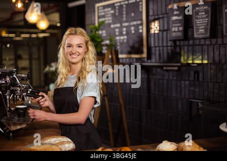 Lächelnde Barista, die am Ladentisch eine Kaffeetasse auf der Espressomaschine mit Portafilter füllt Stockfoto
