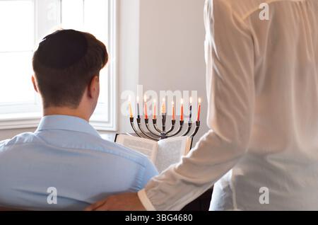 Ein Paar feiert Chanukah mit zündeten Menorah-Kerzen und liest Segen aus der thora Stockfoto