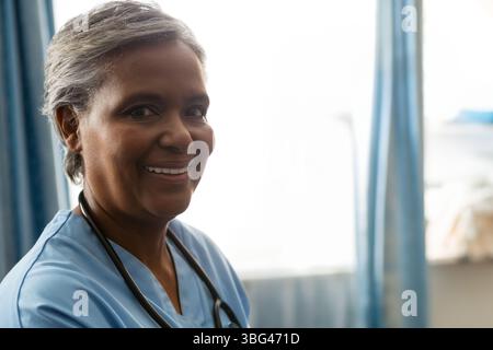 Leitender afroamerikanischer Gesundheitsfachmann, der am Klinikfenster steht, mit Peelings und Stethoskop Stockfoto
