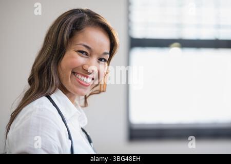 Mittlerer Erwachsener asiatischer Arzt mit Stethoskop stehend in der medizinischen Praxis lächelnd in die Kamera, Kopierraum Stockfoto