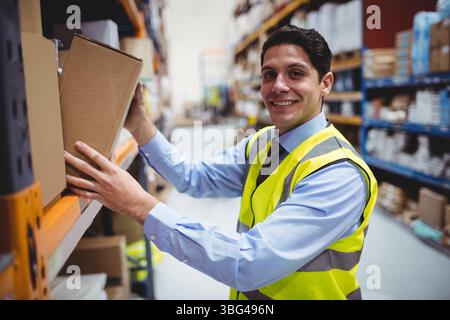Mann, der im Lagerhaus steht, trägt eine gut sichtbare Sicherheitsweste mit Pappkarton und Kopierraum Stockfoto