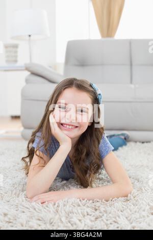Mädchen, das auf einem weißen Teppich in hellem Wohnzimmer liegt, mit blauer Haarschleife Stockfoto