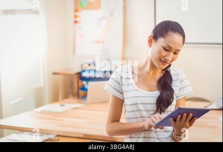 Asiatische Frau, die im Heimbüro steht und ein Tablet am Holzschreibtisch mit Laptop, Kopierraum antippt Stockfoto