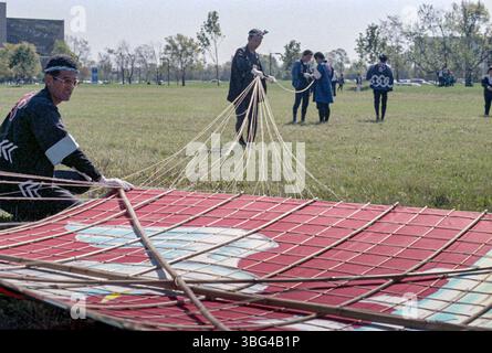 Mehrere japanische Drachenflieger bereiten einen großen Krandrachen für den Flug während einer Drachenkonvention 1983 in Dublin vor. Der Drachen ist ein Herzstück der Veranstaltung und zieht die Aufmerksamkeit der Menge auf sich. Stockfoto