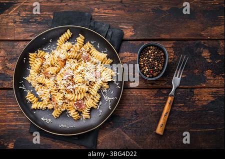 Italienische Carbonara-Pasta mit knusprigen Speckstückchen auf einem Teller. Hölzerner Hintergrund. Draufsicht. Stockfoto