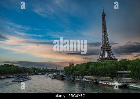 Ein malerischer Blick auf den Eiffelturm, der über der seine in Paris ragt, mit Booten, die am Ufer angedockt sind, und einem lebhaften Himmel über dem Ufer. Stockfoto