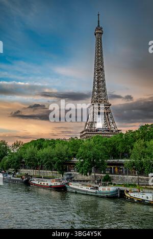 Ein malerischer Blick auf den Eiffelturm, der über der seine in Paris ragt, mit Booten, die am Ufer angedockt sind, und einem lebhaften Himmel über dem Ufer. Stockfoto