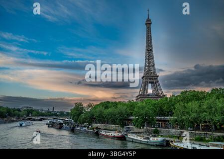 Ein malerischer Blick auf den Eiffelturm, der über der seine in Paris ragt, mit Booten, die am Ufer angedockt sind, und einem lebhaften Himmel über dem Ufer. Stockfoto