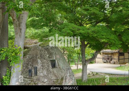 Eine ruhige Szene eines traditionellen japanischen Gartens mit üppigem Grün, verwitterten Felsen und einem Blick auf eine rustikale Struktur. Stockfoto