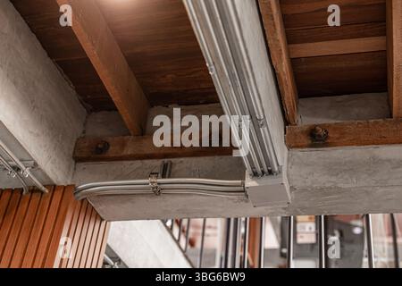 Metallrohrleitung, Rohrleitungssteckverbinder für Stromleitungen an der modernen Holzdecke installiert. Stockfoto