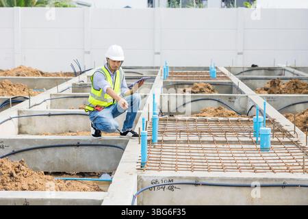 Asiatischer Bauingenieur, japanischer Bauarbeiter, männlich, der die Füße der Fundamente des Rohrhauses überprüft. Stockfoto