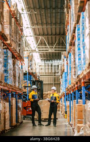 Lagerarbeiter arbeiten zusammen, Mitarbeiterbestandsmitarbeiter im Lagergebäude im Einsatz mit Sicherheitsanzug, vertikaler Schuss Stockfoto