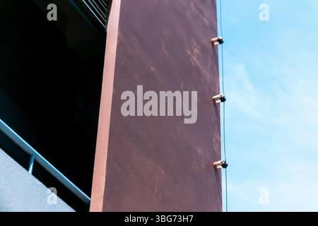Eine abstrakte Ansicht einer modernen architektonischen Wand mit einer einzigartigen braunen Textur vor einem hellblauen Himmel, mit klaren Linien und geometrischem Mini Stockfoto