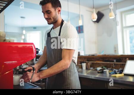 Männlicher Barista, der den Portafilter der roten Espressomaschine auf der Theke im Coffee Shop mit Tablet bedient Stockfoto