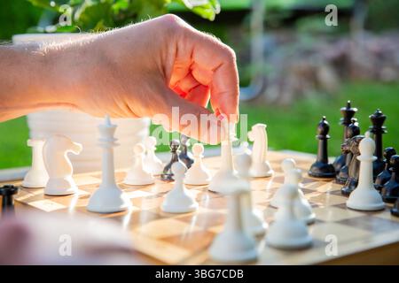 Nahaufnahme eines alten Holzschachbretts während eines Sommerspiels. Ein Vater hält ein königliches Stück, das Strategie und nachdenkliches Spiel symbolisiert. Stockfoto