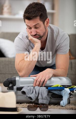 Trauriger männlicher Tourist, der auf einem gepackten Koffer sitzt Stockfoto